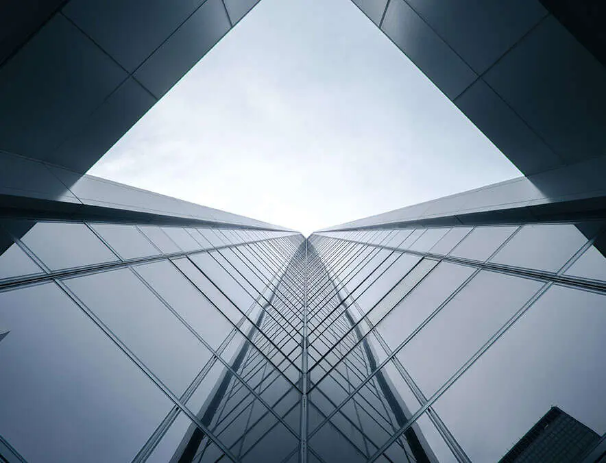 Looking up at a modern glass skyscraper against a cloudy sky.